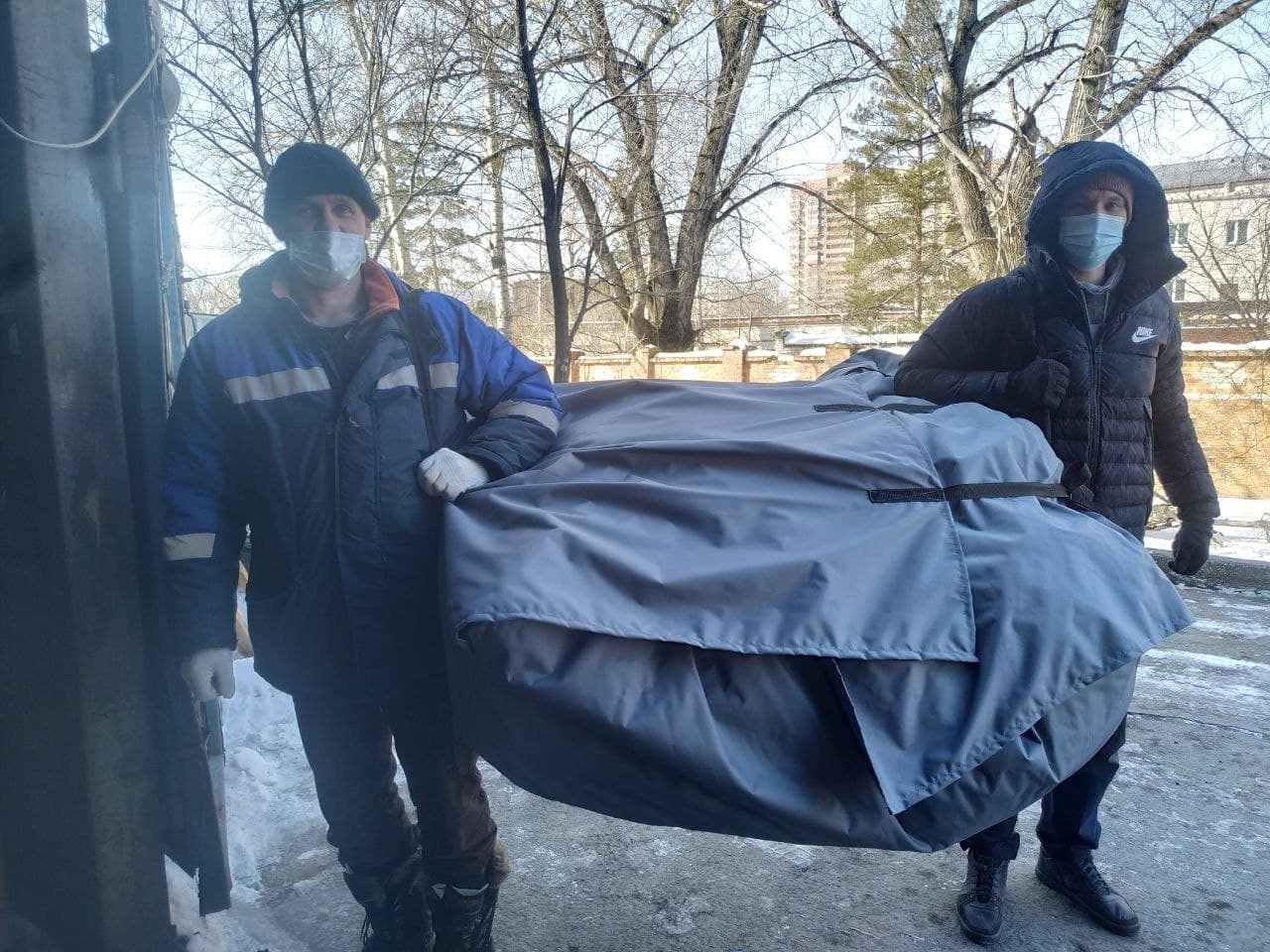 Двое рабочих несут сложенную палатку в транспортировочной сумке